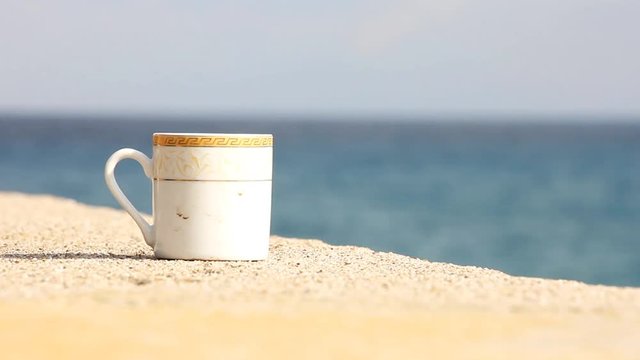 Coffee mug with a traditional Greek ornament stands on the parapet of the Mediterranean sea embankment.