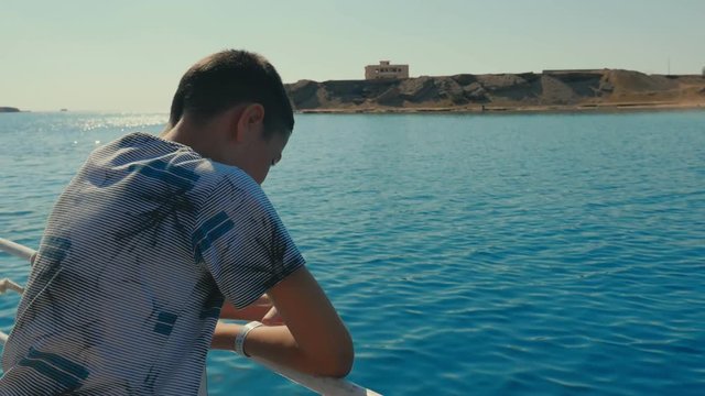 Small boy enjoys the rippling sea waves leaning on touristic ship rails in Egypt  