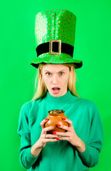 Surprised blonde girl in Leprechaun costume holds pot with gold. Green hat. Leprechaun. Pot with...