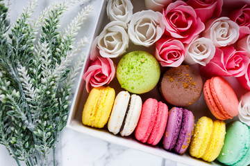Box with colorful pastel macaroons and flowers on white marble background. Coffee break with sweets. Valentines day, Spring background. Top view, 