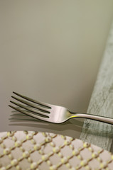 close up of a chrome fork with a silver plate on one side on a transparent glass table