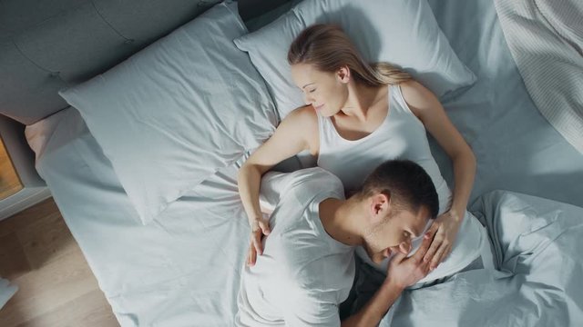 Happy Young Couple Cuddling Together in the Bed, Young Woman is Pregnant, Loving Partner Leans and Listens to a Baby Moving and it's Heartbeat in the Belly. Tender and Loving Moments of Family Life.