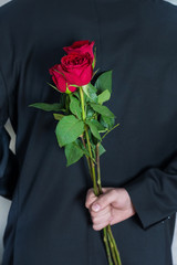 Man holding red rose flowers behind his back. Surprised gift for woman. Romantic and valentines day holiday concept. Close up, selective focus