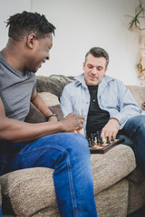 A gay couple enjoying time indoors at home, playing chess. 