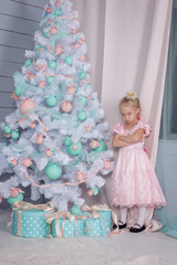 Portrait of an offended and frustrated European little blonde Princess girl with a crown in a beautiful dress and opening gifts in a decorated Studio  with toys and a Christmas tree