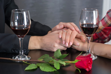 Young couple hands on restaurant table with two glasses of red wine and roses. Romantic couple holding each others hand at dinner in a luxury restaurant. Valentines day concept