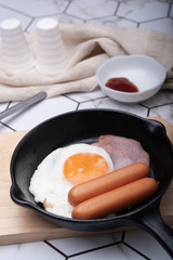 Breakfast fried egg with sausage and ham on a iron pan served with tomato sauce in the morning