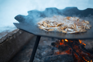Cooking fish in a flat pan on the bonfire outdoor of winter