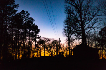 Power lines leading into the woods at sunset