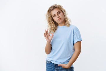 You are good, not bad at all. Portrait of impressed and proud cool swag young girl with short blond curly hair frown and pursing lips as showing okay gesture in approval and like gesture