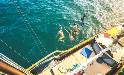 Aerial view of happy millenial friends jumping from sailboat on sea ocean trip - Rich guys and...