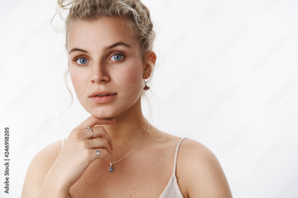 Wall mural Close-up shot of thoughtful and sensual blond female european model with blue eyes in light dress touching chin soft and tender expressing tenderness and gentle feelings over white background - Wall murals