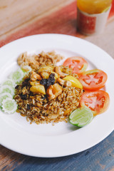 Close up Thai Pineapple Fried Rice topping with raisin, cashews and dried shredded pork. Served with cucumber and tomato.
