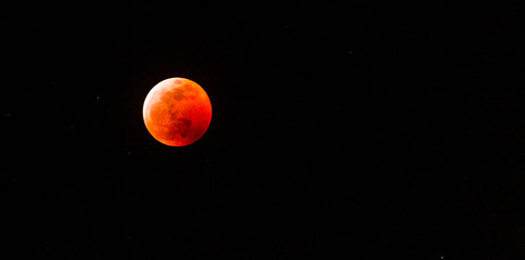 The full Lunar Eclipse in January of 2019 shows the moon in full eclipse and pictures a orangey, red moon glowing in the sky with a section on the edge with whiteish light from the glow of the sun. 