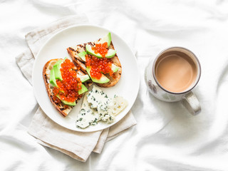 Delicious breakfast or snack - red caviar, avocado sandwiches and blue cheese on light background, top view