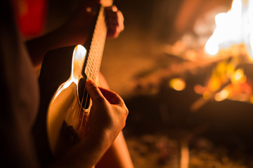 A female musician playing guitar outside, sitting next to a fire. Relaxation.