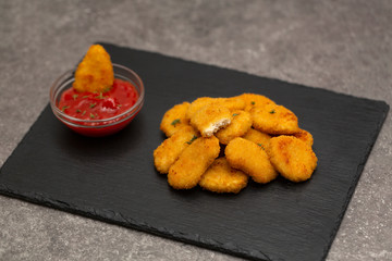Fried crispy chicken nuggets with ketchup on black board.