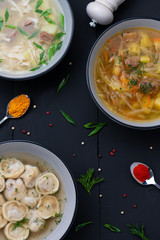 Set soups. Russian cuisine. vegetables soup with meat and chopped cabbage, soup with meat and homemade noodles, pelmeni on black wooden background. Top view.