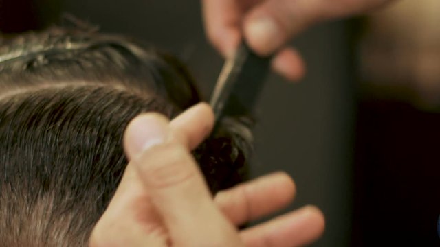 Hand haircutter combing wet hair and using hairdressing scissors for cutting close up. Hairdresser making male hairstyle with comb and hairdressing scissors in barber shop