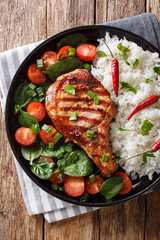 Healthy grilled pork steak with rice and fresh vegetables close-up on a plate. Vertical top view