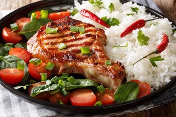 grilled pork chop cutlet with rice and fresh vegetable salad close-up on a plate. horizontal