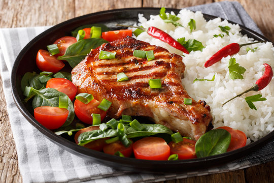 Homemade dinner of grilled pork chop with rice and fresh vegetable salad close-up. horizontal