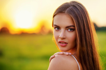 Beautiful young woman on nature over summer sunset.