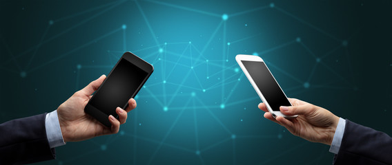 Close up of two hands holding smartphones to each other, wireless connection concept