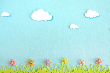appliqué clouds, grass and wooden flowers on blue textured paper. copy space..