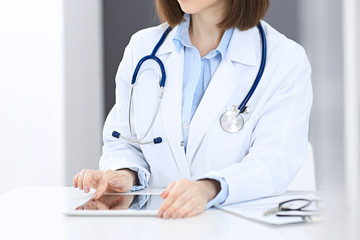 Doctor woman at work. Female physician using tablet computer while sitting at the desk in clinic or hospital. Medicine and healthcare concept for advertising