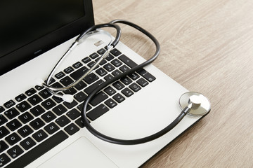 Modern medical technology and sofware advances concept. Doctor's working table with stethoscope acoustic device, laptop keyboard close up on wooden desktop. Copy space, background, top view, flat lay.