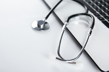 Modern medical technology and sofware advances concept. Doctor's working table with stethoscope acoustic device, laptop computer keyboard close up. Copy space, background, top view, flat lay.