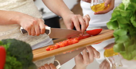 Closeup of human hands cooking in kitchen. Mother and daughter or two female friends cutting vegetables for fresh salad. Friendship, family dinner and lifestyle concepts
