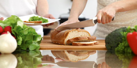 Closeup of human hands cooking in kitchen. Mother and daughter or two female friends cutting bread for dinner. Friendship, family and lifestyle concepts