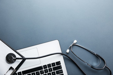 Modern medical technology and sofware advances concept. Doctor's working table with stethoscope acoustic device, laptop computer keyboard close up. Copy space, background, top view, flat lay.
