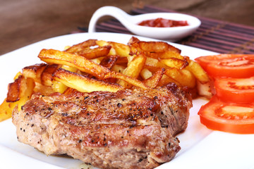 Grilled free-range beef steak with potato free, fresh tomatoes and sauce on a brown stone background