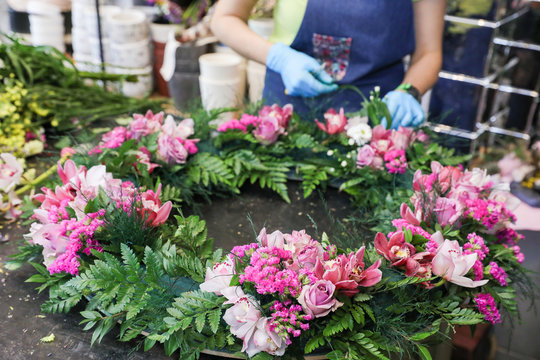 The florist creates a wreath of exotic flowers in pink tones from orchids, roses, and other flowers, herbs.