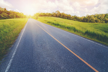 Highway road up hill through green grass field under white clouds on blue sky in summer day. Road...