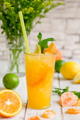 Juiced cocktail in glass and fresh fruits with leaves on white wooden background, orange, lemon, tangerine and lime vitamin drink or cocktail. 