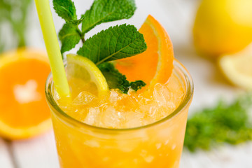 Juiced cocktail in glass and fresh fruits with leaves on white wooden background, orange, lemon and lime vitamin drink or cocktail. Closeup.