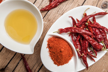 Olives oil and red chili pepper in bowl on wood rustic background, top view