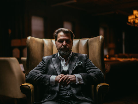 Pensive elegant bearded businessman thinks about something important while sitting in the leather armchair in living room