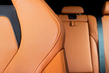 Part of red perforated leather car seat with the unfocused car interior in the background