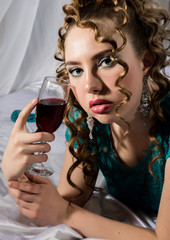mysterious young curly woman resting on the bed and drinks red wine