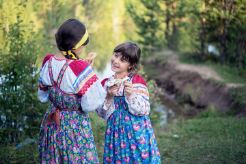 Two smiling girls in dresses in the forest with mushrooms in their hands.