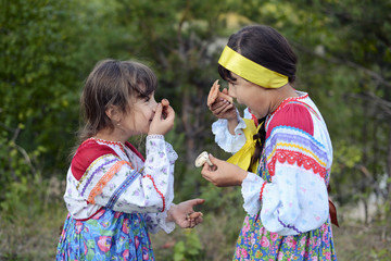 Two smiling girls in dresses in the forest with mushrooms in their hands.