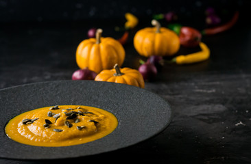 Pumpkin orange cream soup in black plate. Dark photo