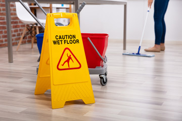 Cleaner Standing With Mop And Caution Wet Floor Sign