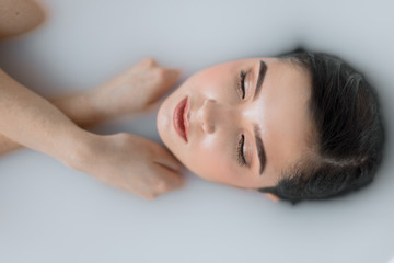 People, resort and recreation concept. Good looking natural young woman rests in milky aroma bath with closed eyes, enjoying recreation time in spa resort