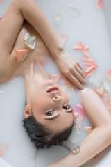 Obraz na płótnie Canvas People, resort and recreation concept. Good looking natural young woman rests in aromatic milky bath with flower petals, resting in spa resort